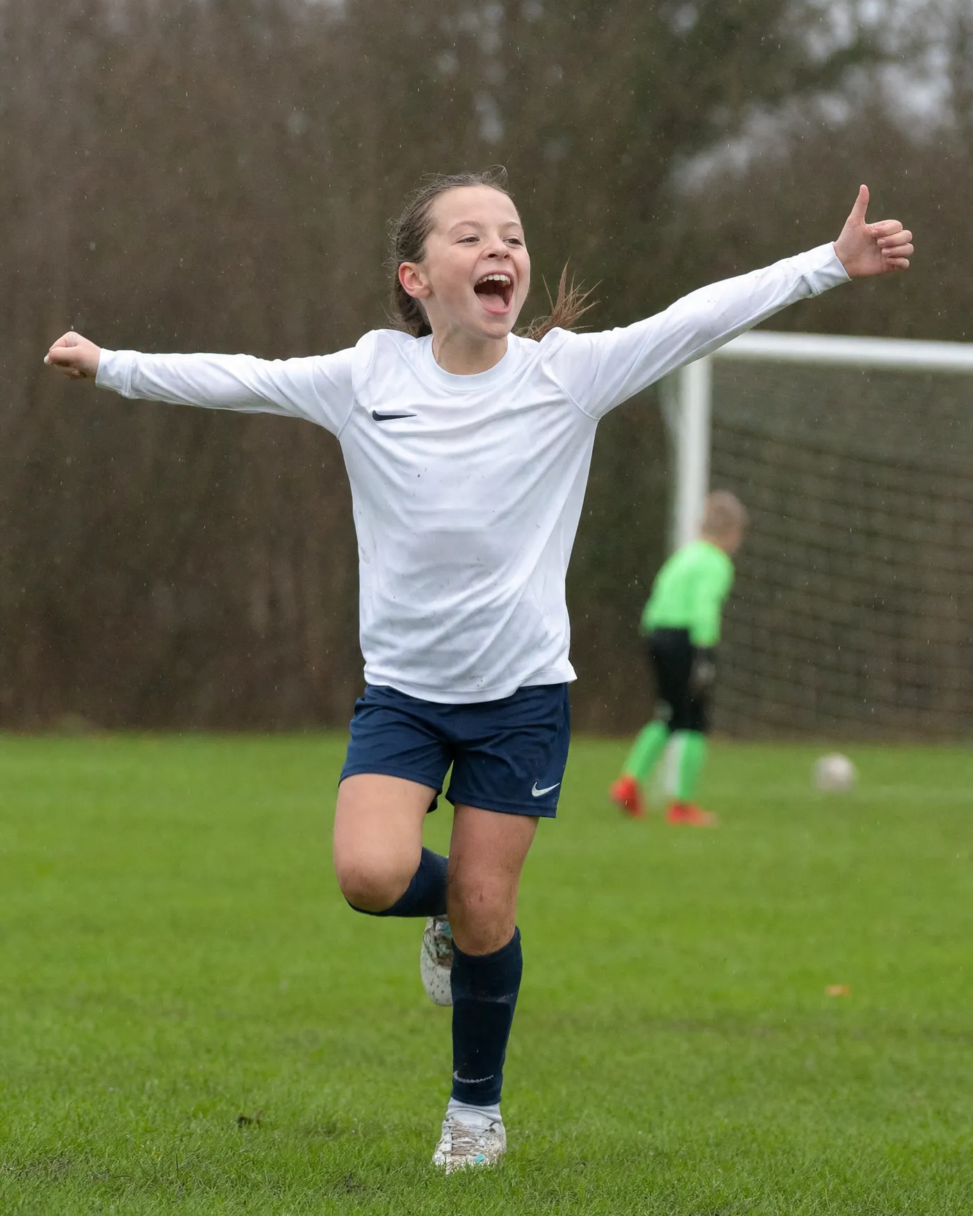 A young player celebrating a goal on a wet pitch